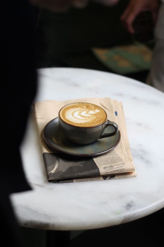 A steaming cappuccino on a newspaper atop a marble table, perfect for mornings.