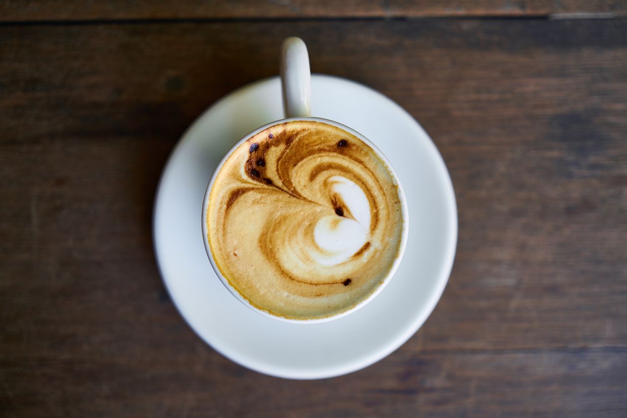 Top view of a coffee cup with intricate latte art on a white saucer.
