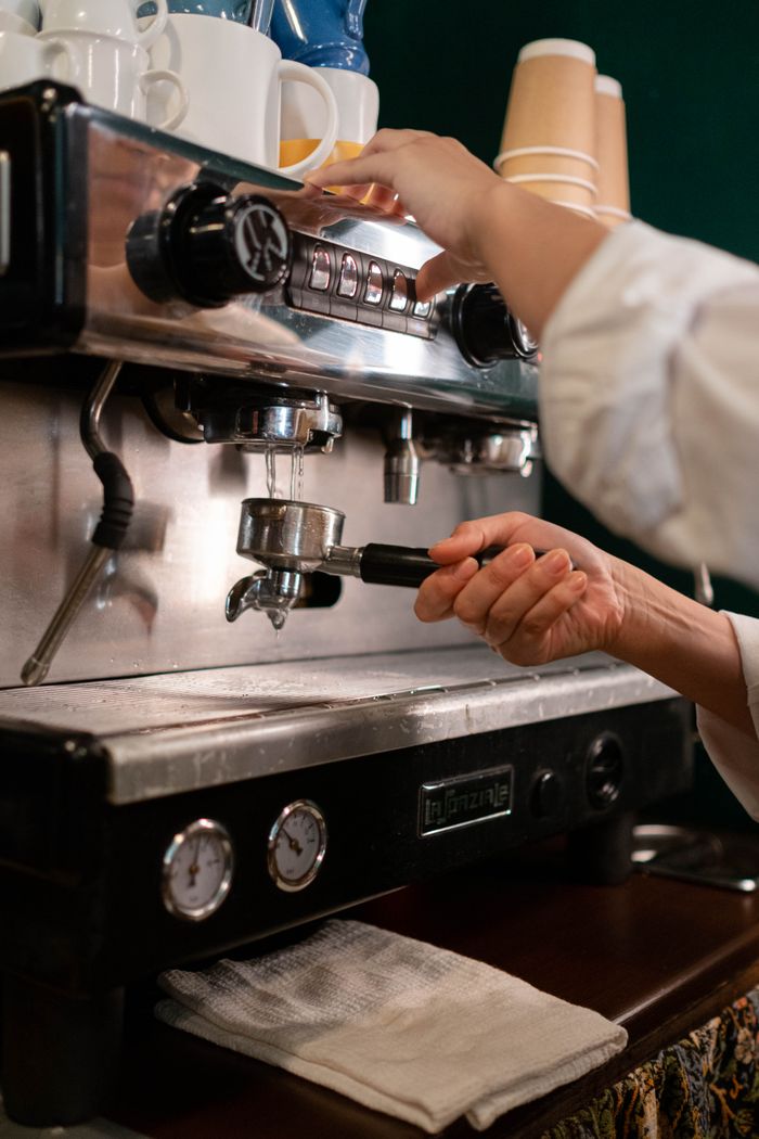 Hands of a barista operating an espresso machine, preparing coffee in a cozy cafe setting.